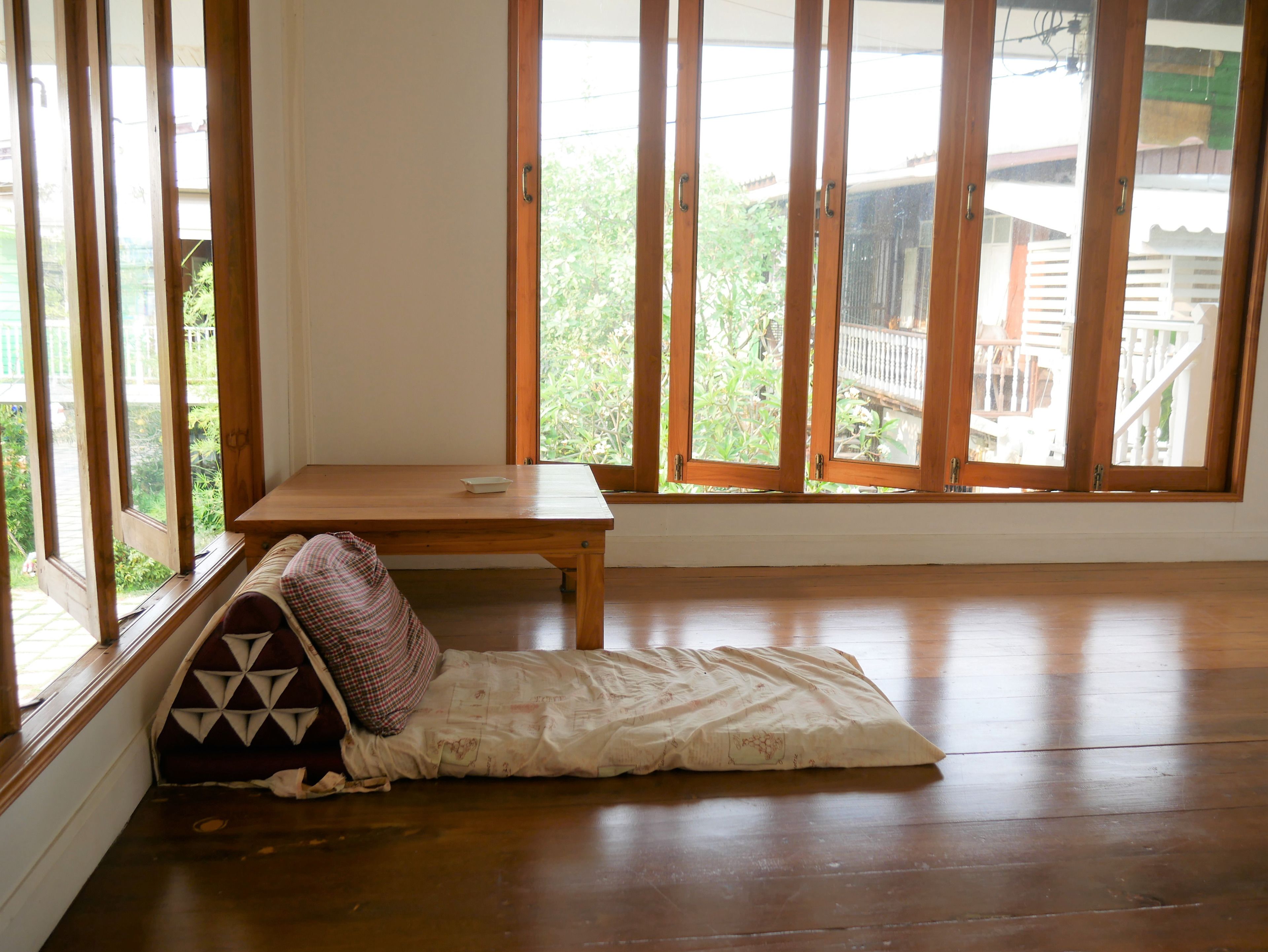 A room with a wooden floor, a small wooden table, and a window with a view of greenery and a wooden deck outside.