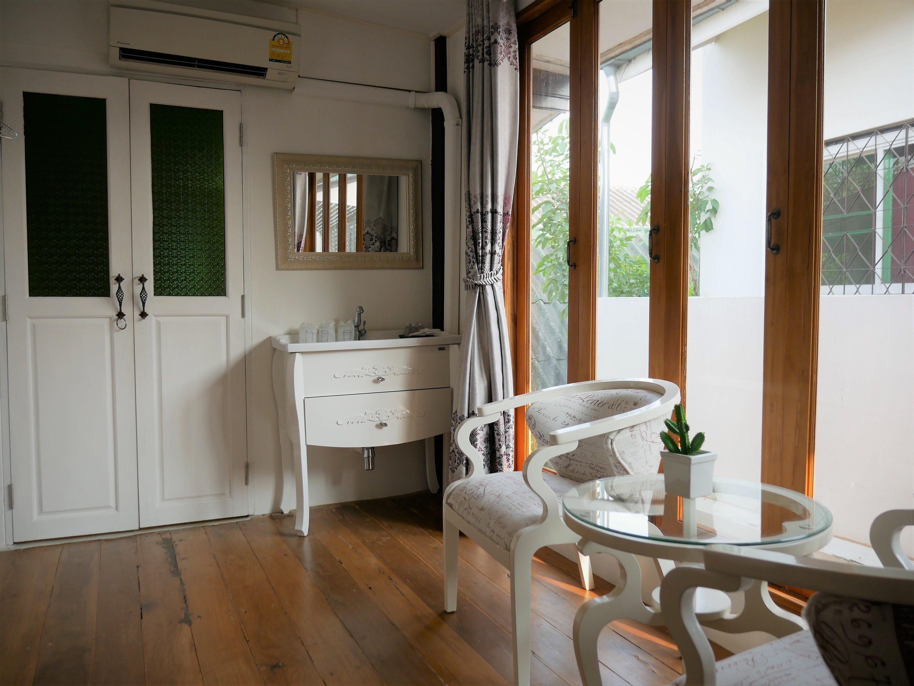 A room with a white dresser, a mirror, a small table with a glass top, and a chair.