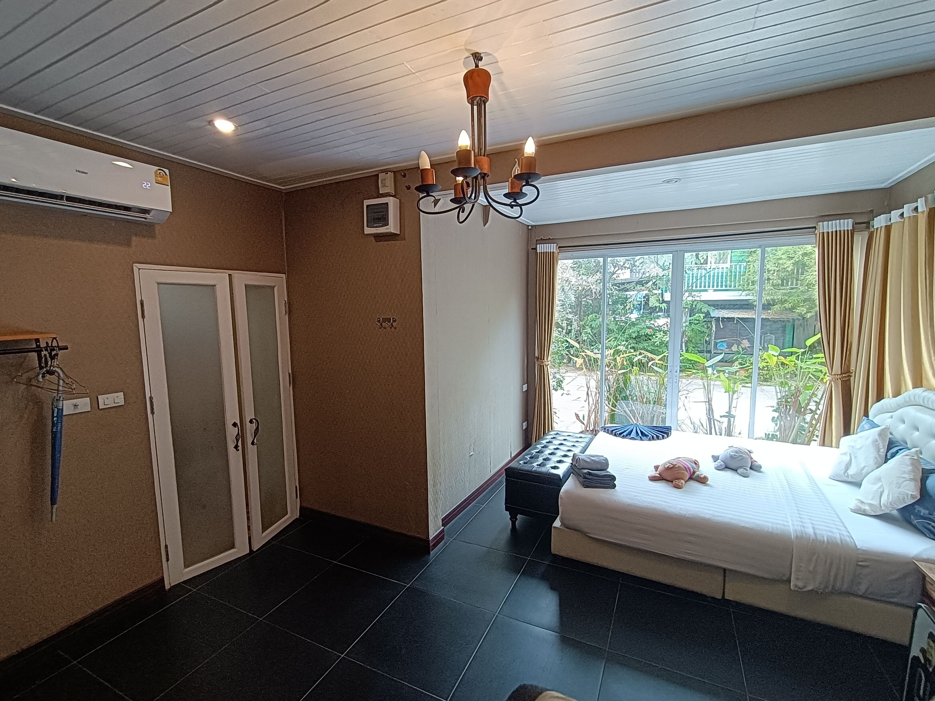 A bedroom with a large bed, a chandelier, a window with curtains, a door, and an air conditioning unit.