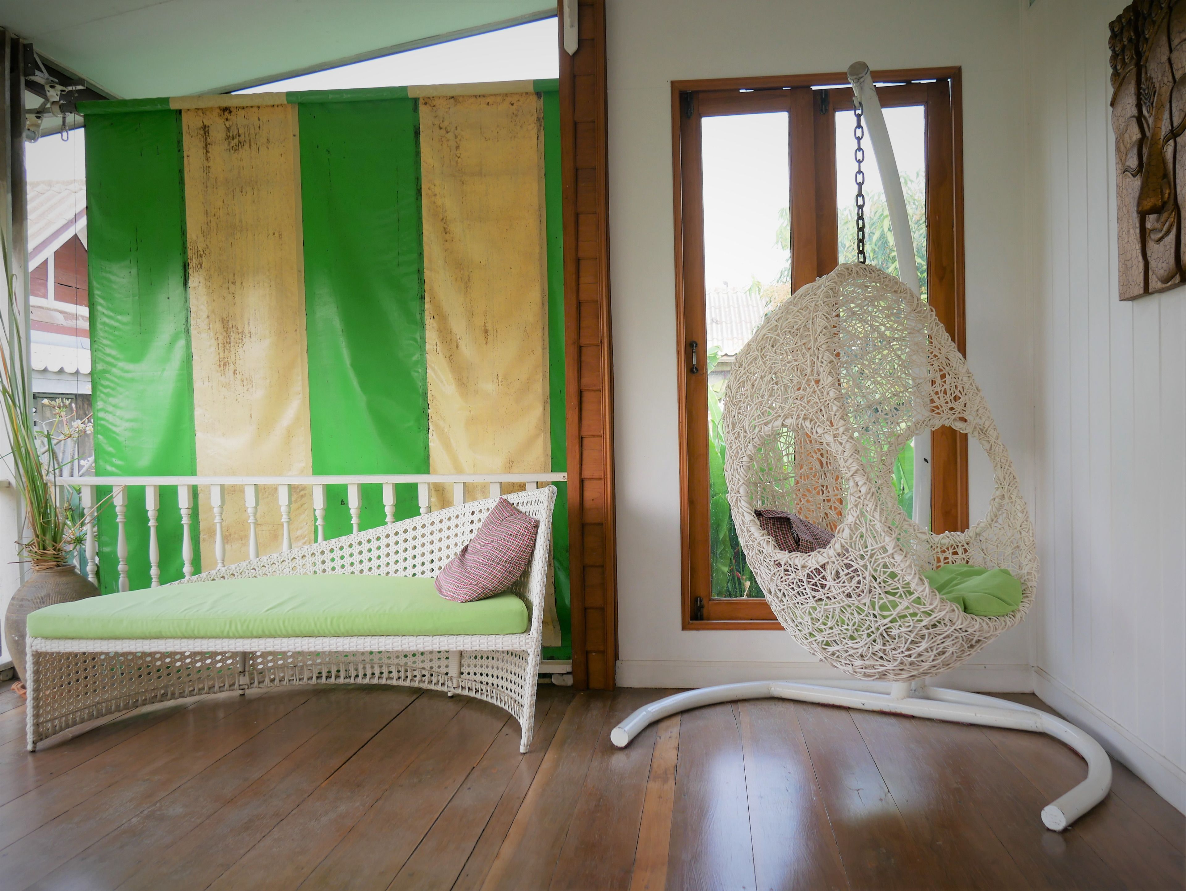 A wicker sofa with a green cushion and a hanging chair with a woven seat.