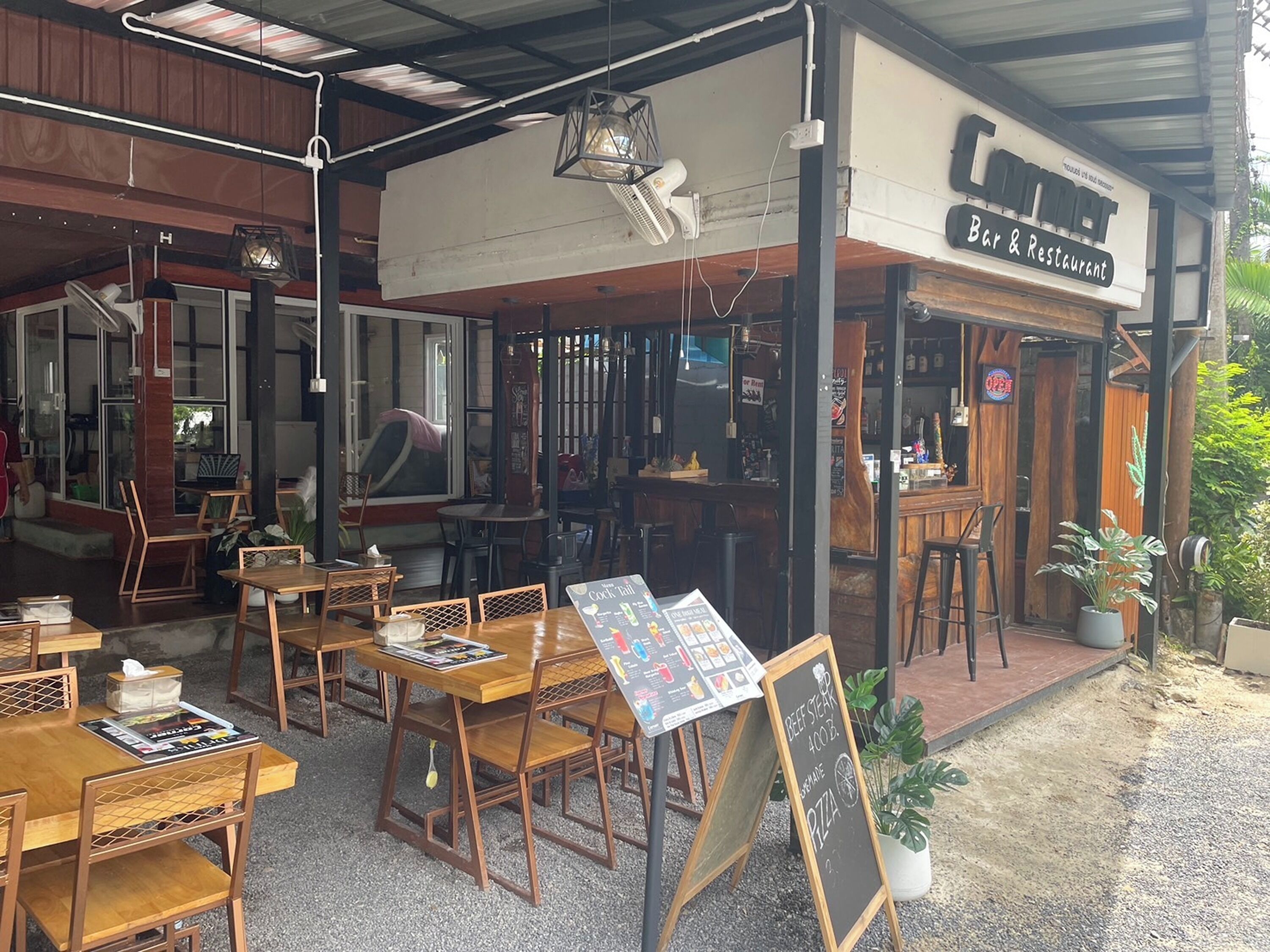 A restaurant with outdoor seating, a chalkboard menu, and a sign indicating it serves beef steak and pizza.