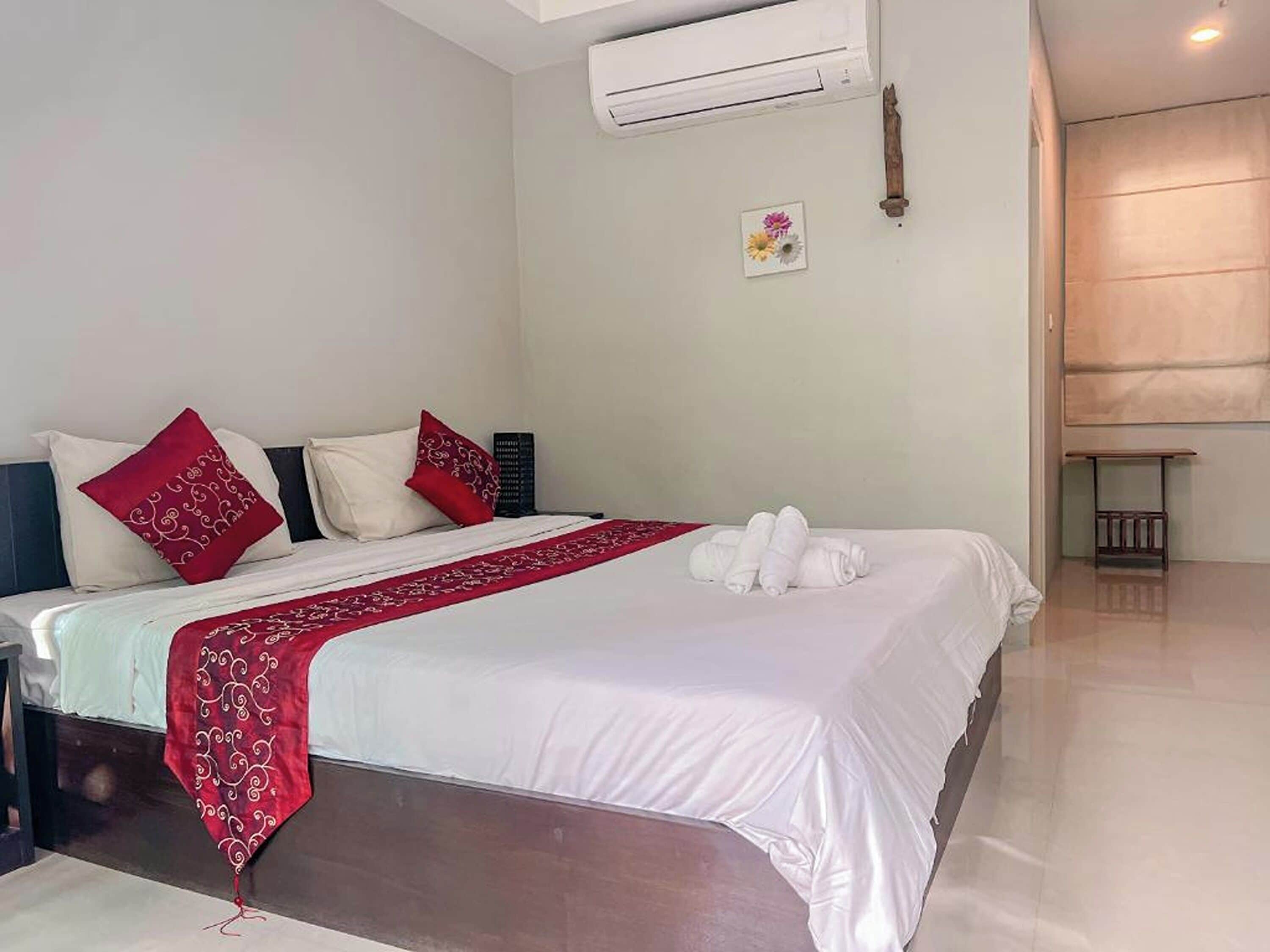 A neatly made bed with white and red bedding, a small bedside table, and an air conditioning unit on the wall.