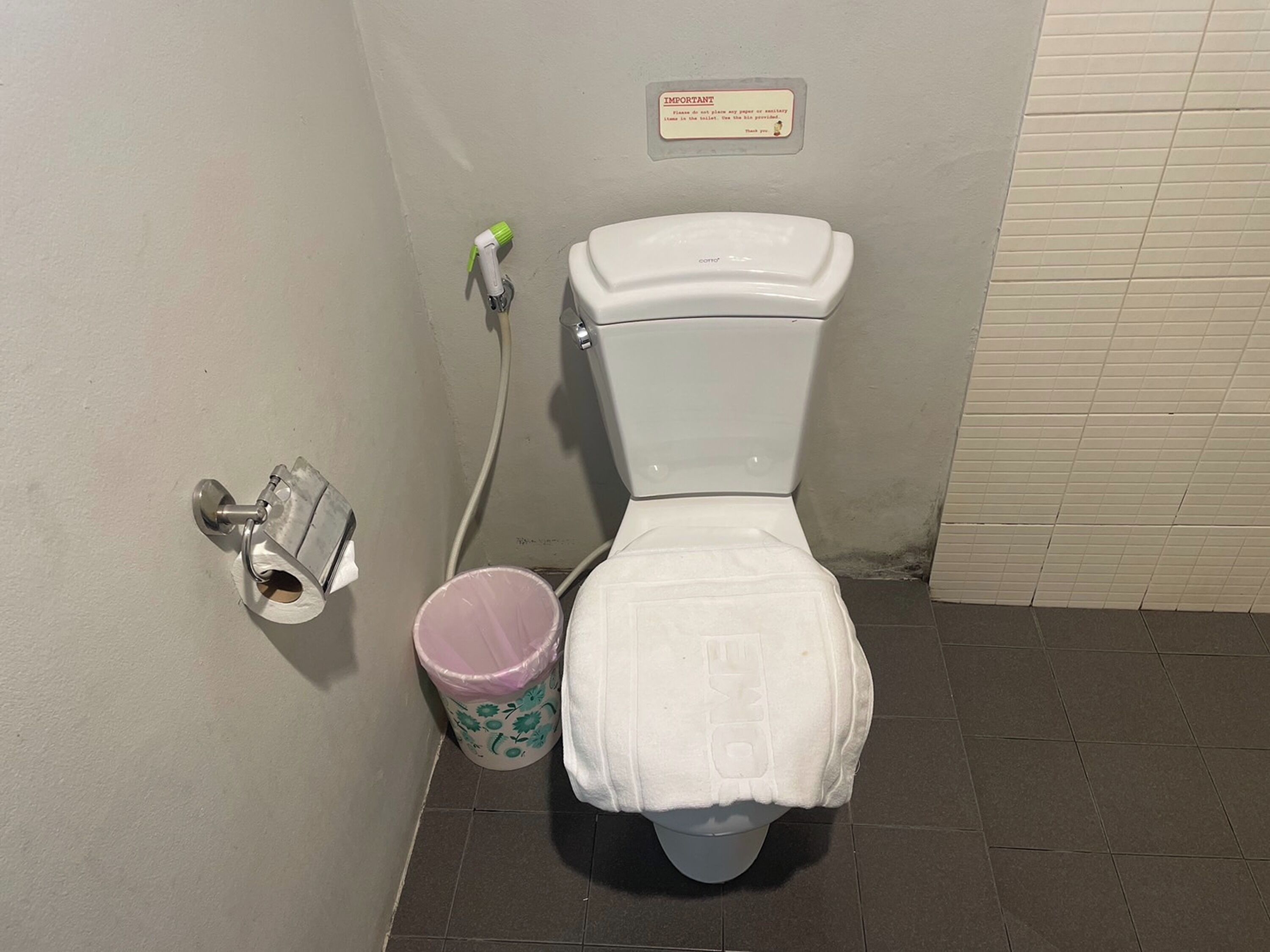 A bathroom with a toilet, a trash can, and a paper towel dispenser.