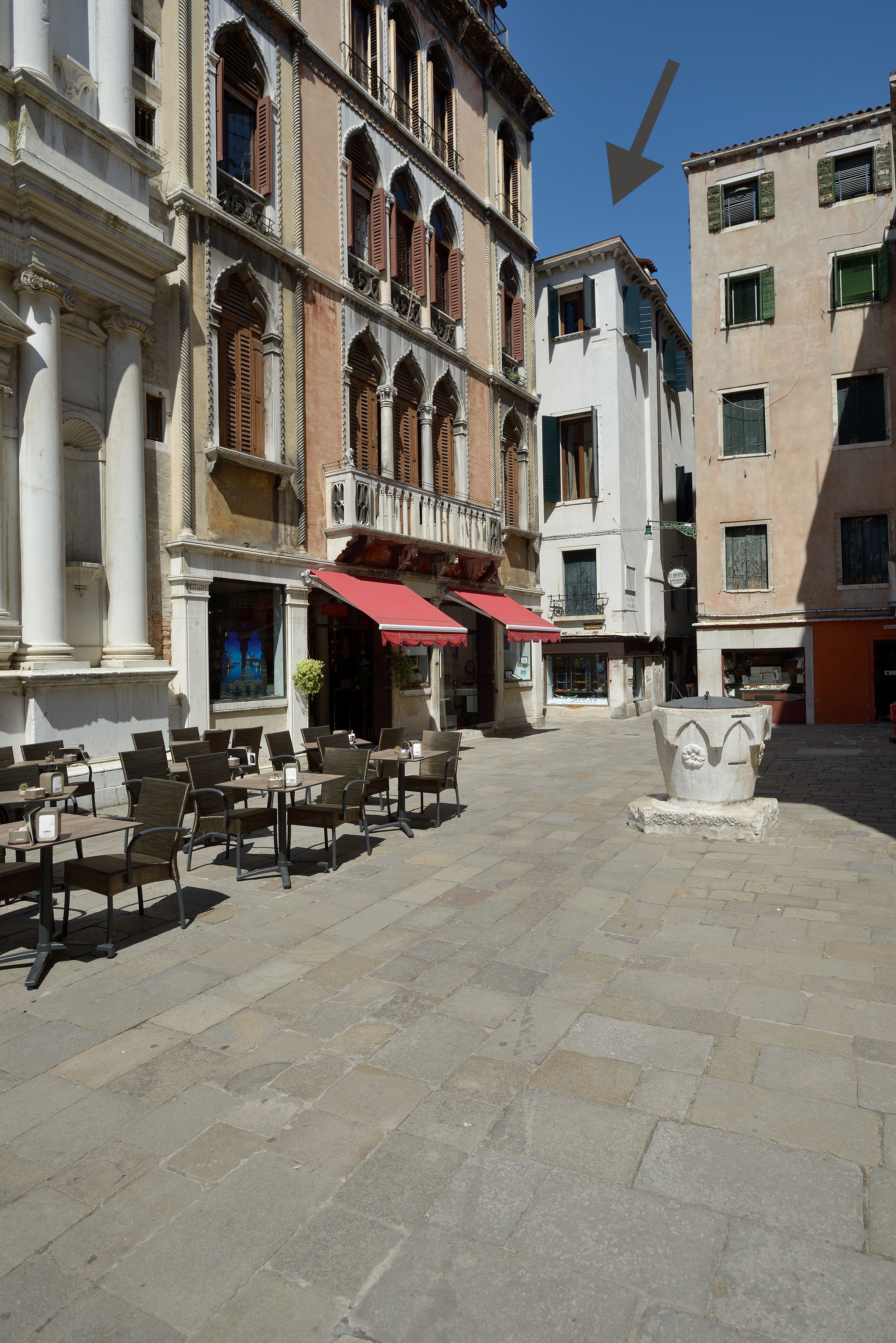 Un área de café al aire libre con suelo de piedra, asientos exteriores y una gran maceta decorativa de piedra.