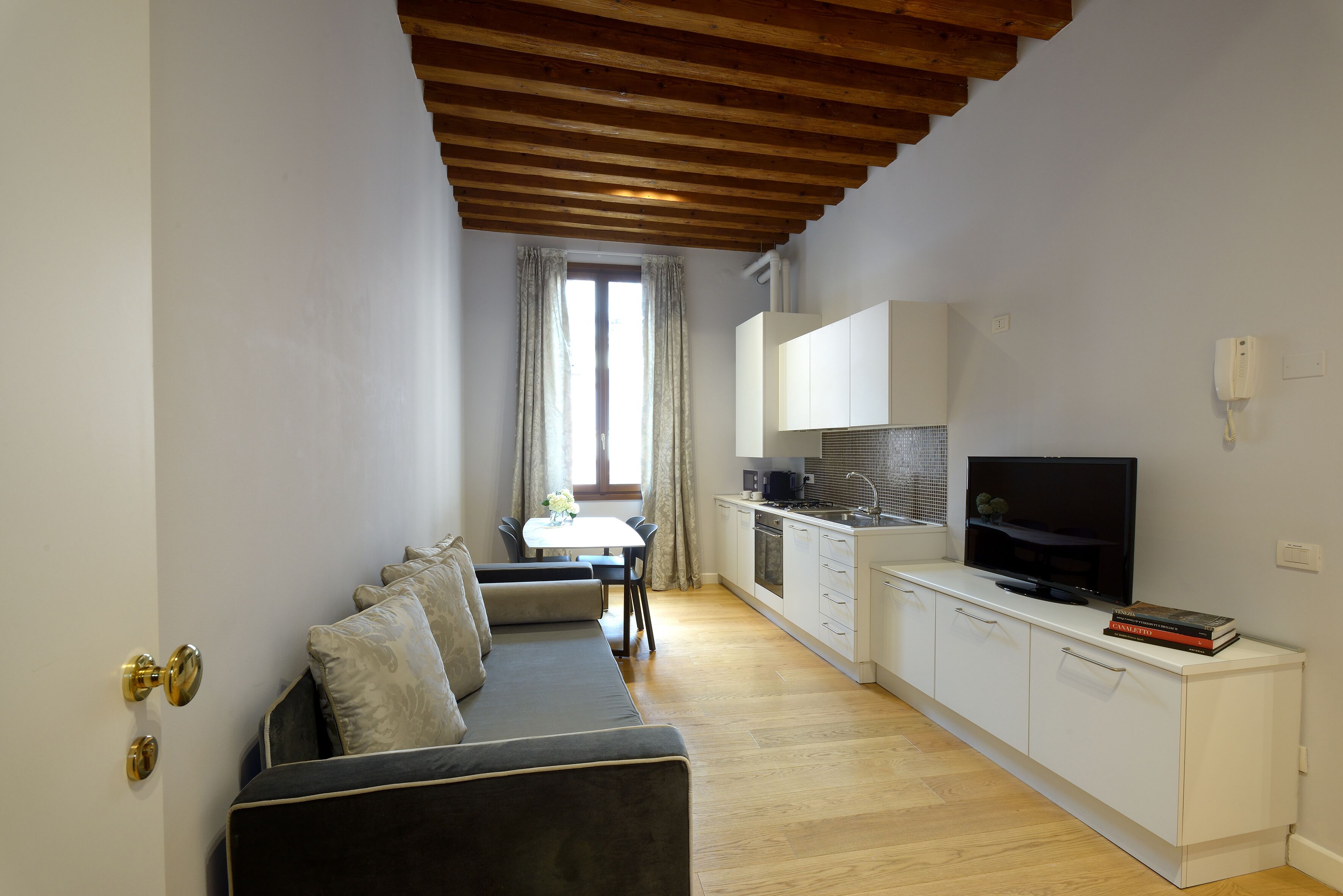 Un ambiente compatto con divano, tavolo da pranzo, angolo cottura e televisione.