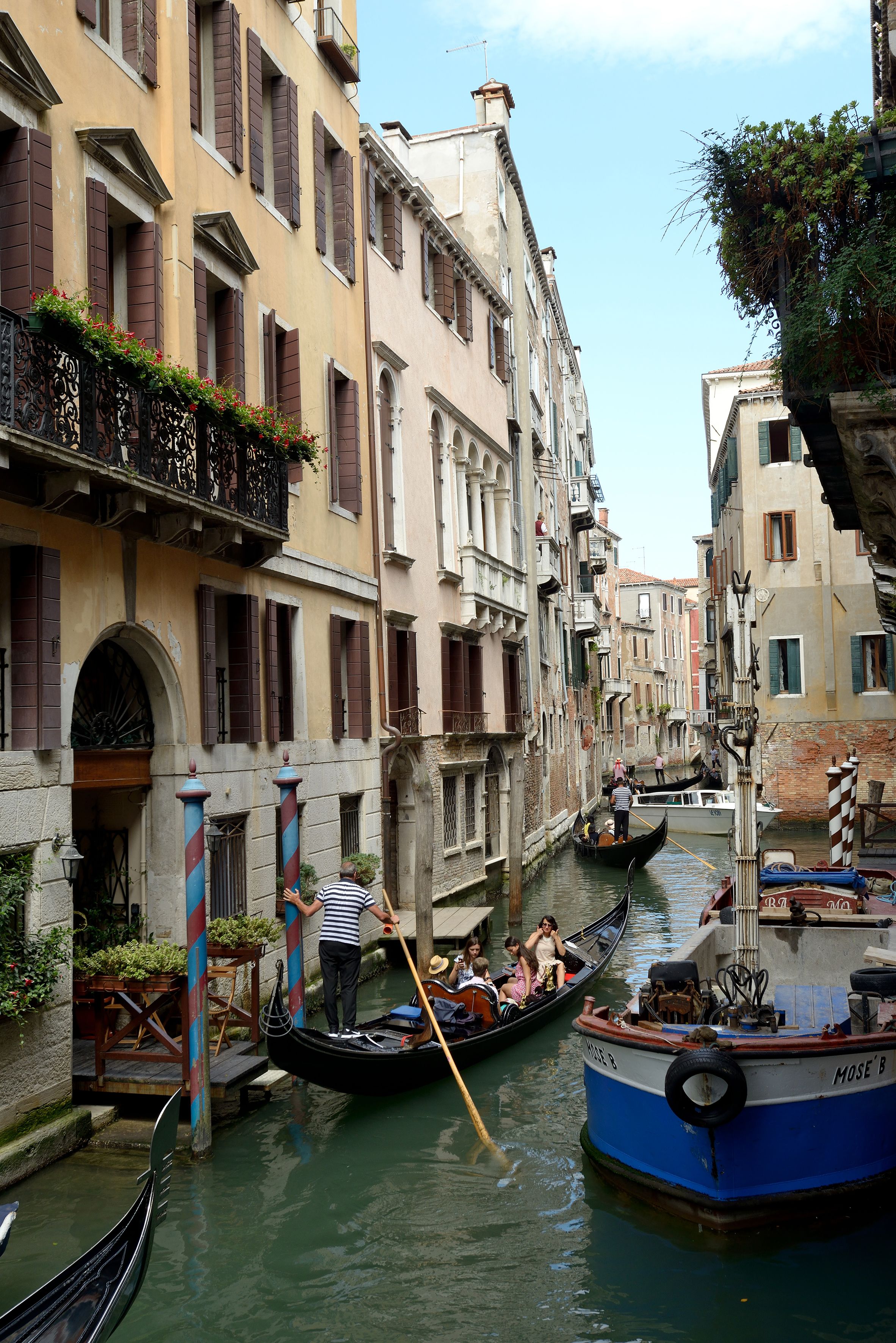 Un canal estrecho con góndolas y barcos, rodeado de edificios históricos con balcones y persianas.