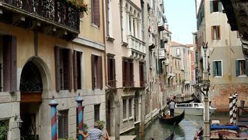 Un canal estrecho con góndolas y barcos, rodeado de edificios históricos con balcones y persianas.