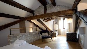 A bedroom with a wooden ceiling, a stone wall, a bed with rolled towels, a chair, and a small table. - Residence La Fenice (Venice)