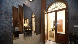 A hallway with a stone wall, a wooden door, and a mirror reflecting a room with a table and chairs. - Residence La Fenice (Venice)