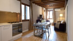 A kitchen with a gas stove, oven, and white cabinets. There is a dining table with chairs and a sofa in the adjacent living area. - Residence La Fenice (Venice)