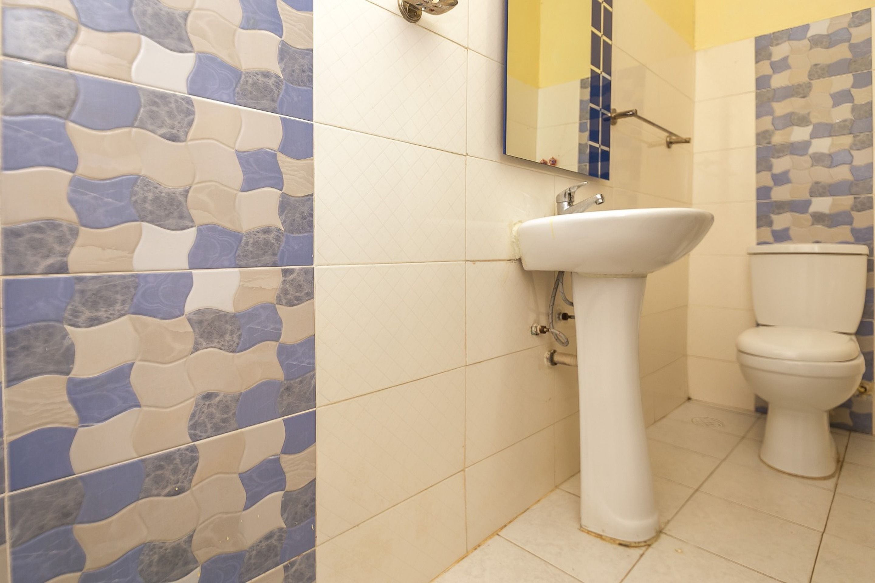 A bathroom with a white sink, a toilet, and tiled walls with a blue and beige pattern.