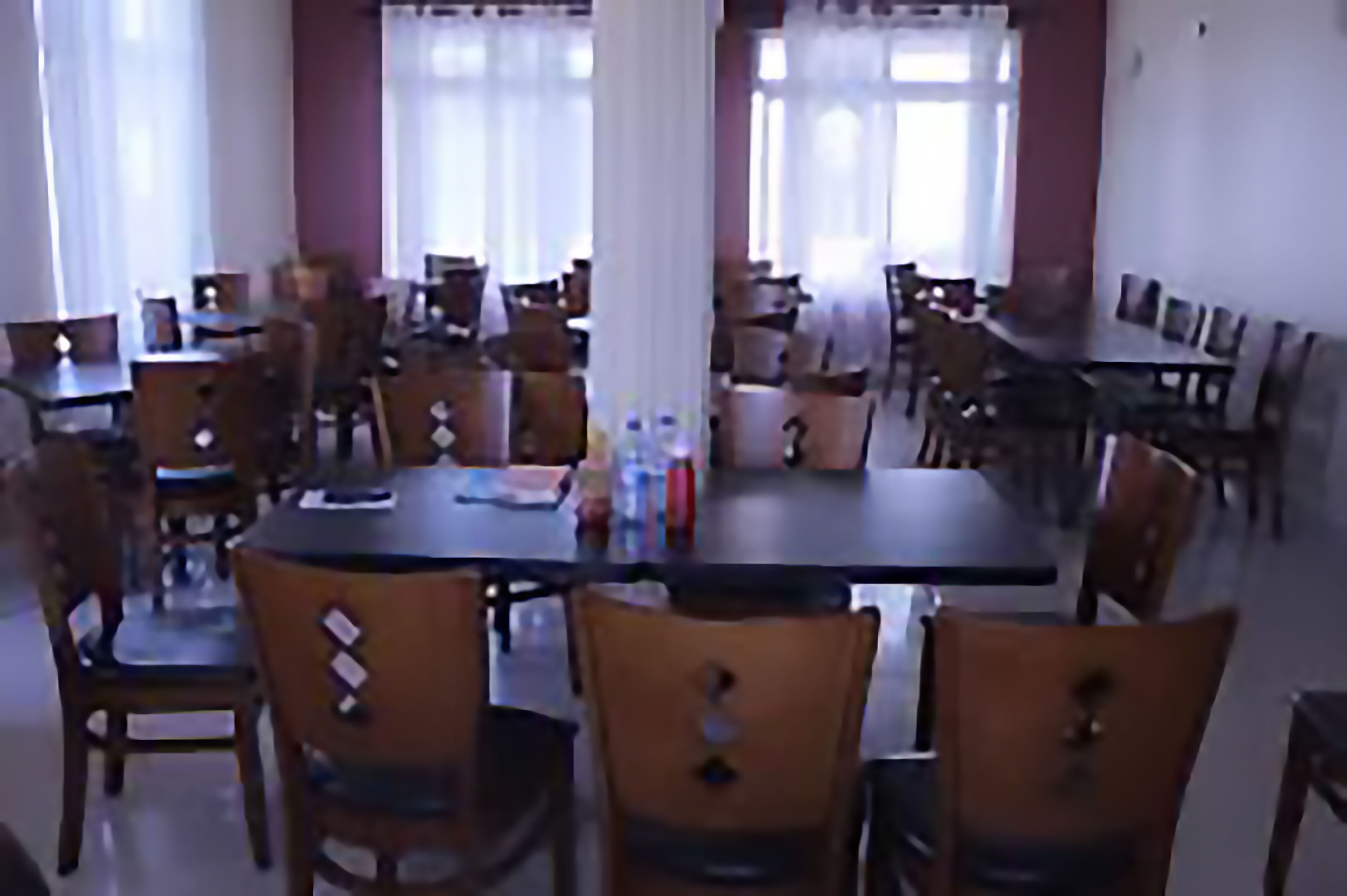 A dining area with multiple tables and chairs, large windows with curtains, and a clean, organized layout.