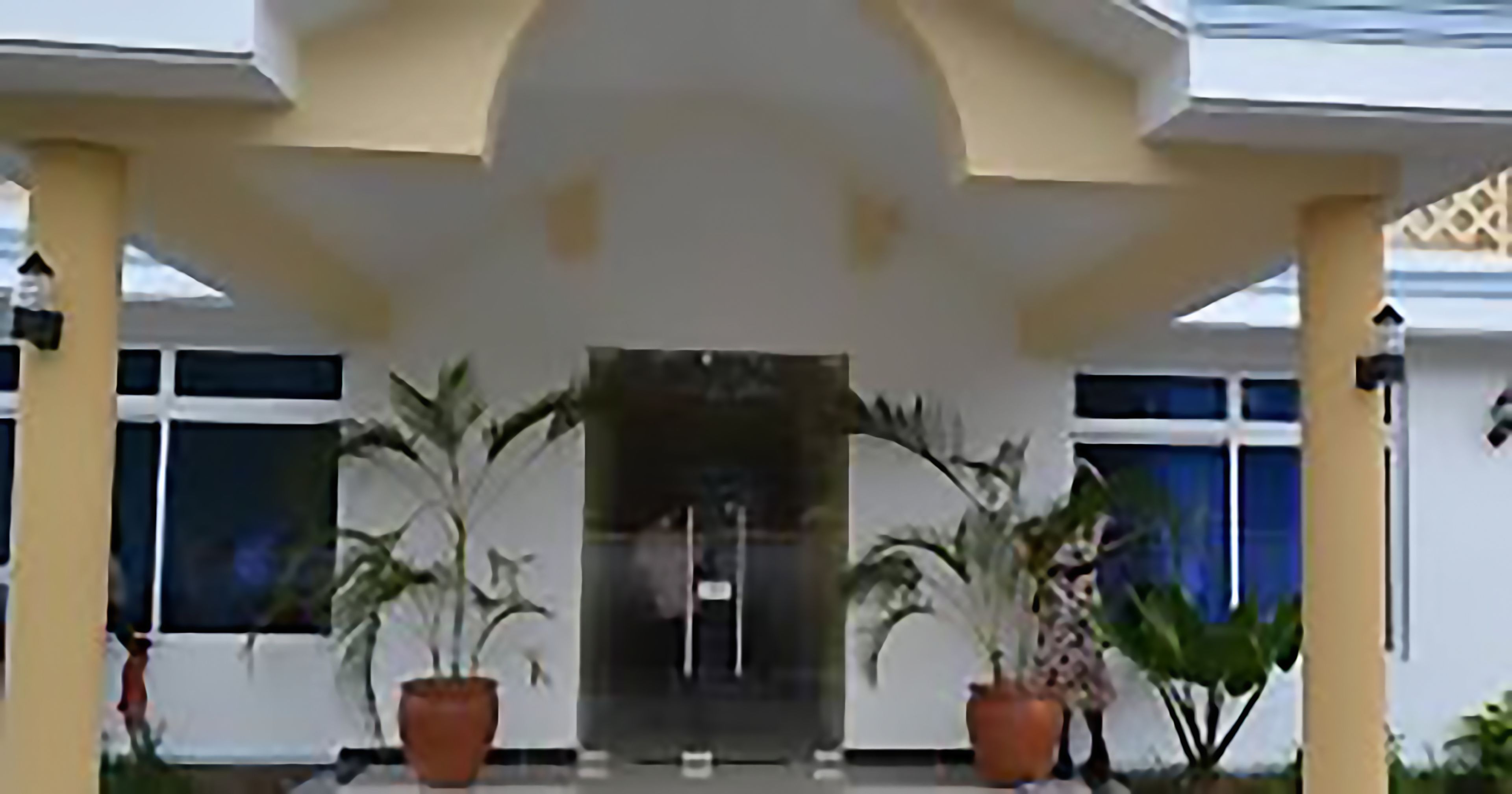 Une entrée d’immeuble avec un porche abrité, des plantes en pot et une vue dégagée sur l’intérieur du bâtiment.