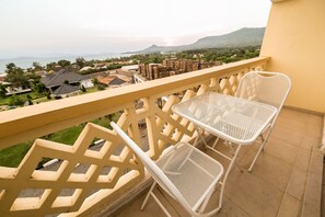 A balcony with white metal chairs and a table, overlooking a residential area with houses and a mountain in the distance.