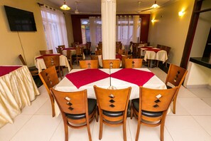 A dining area with round tables, wooden chairs, and white tablecloths.