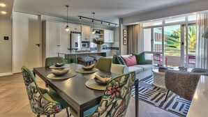 A modern kitchen with white cabinets, a dining area with a wooden table and chairs, and a living area with a sofa and a coffee table. - 437 St Martini Gardens (Cape Town)