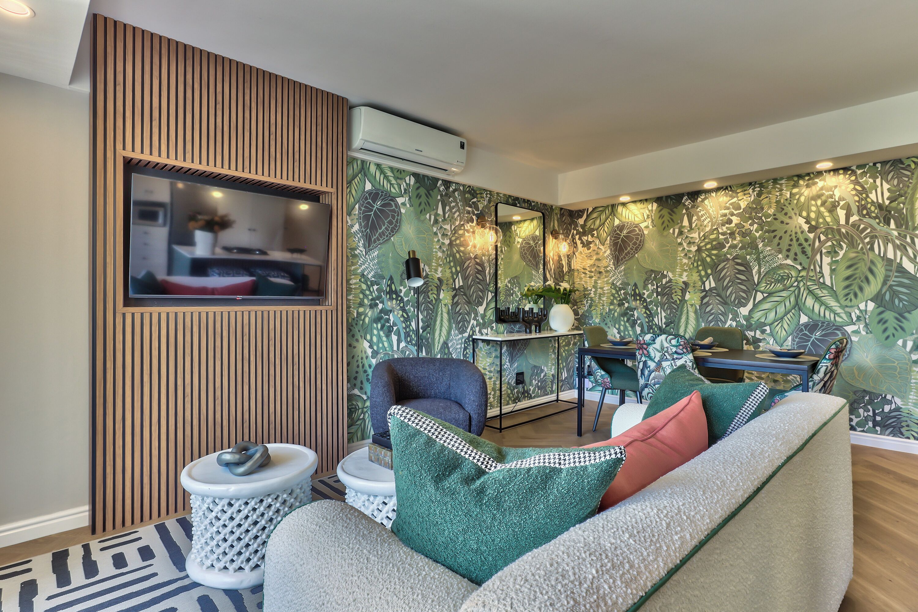 A modern living room with a sofa, a chair, and a small table. There is a wooden panel on one wall and an air conditioning unit above it.