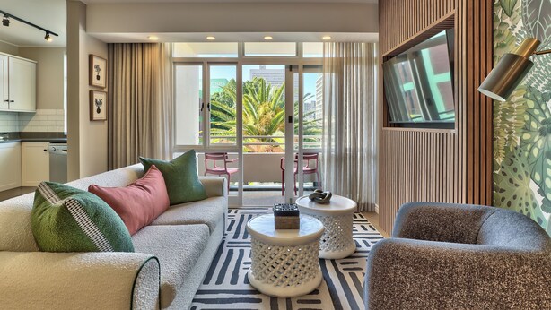 A modern living room with a sofa, two side tables, a TV, and a view of the outdoors. - 437 St Martini Gardens (Cape Town)