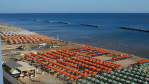 A beach with rows of orange and green umbrellas, a clear sky, and calm water. - Hotel Embassy Pesaro (Pesaro)