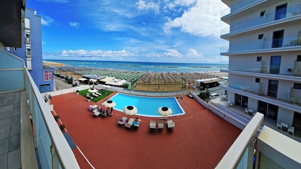 A rooftop pool with sun loungers and umbrellas, overlooking a beach with umbrellas and people. - Hotel Embassy Pesaro (Pesaro)