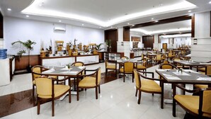 Ein großzügiger Hotel-Speisesaal mit mehreren Tischen und Stühlen, einem Empfangsbereich und modernem Interieur.