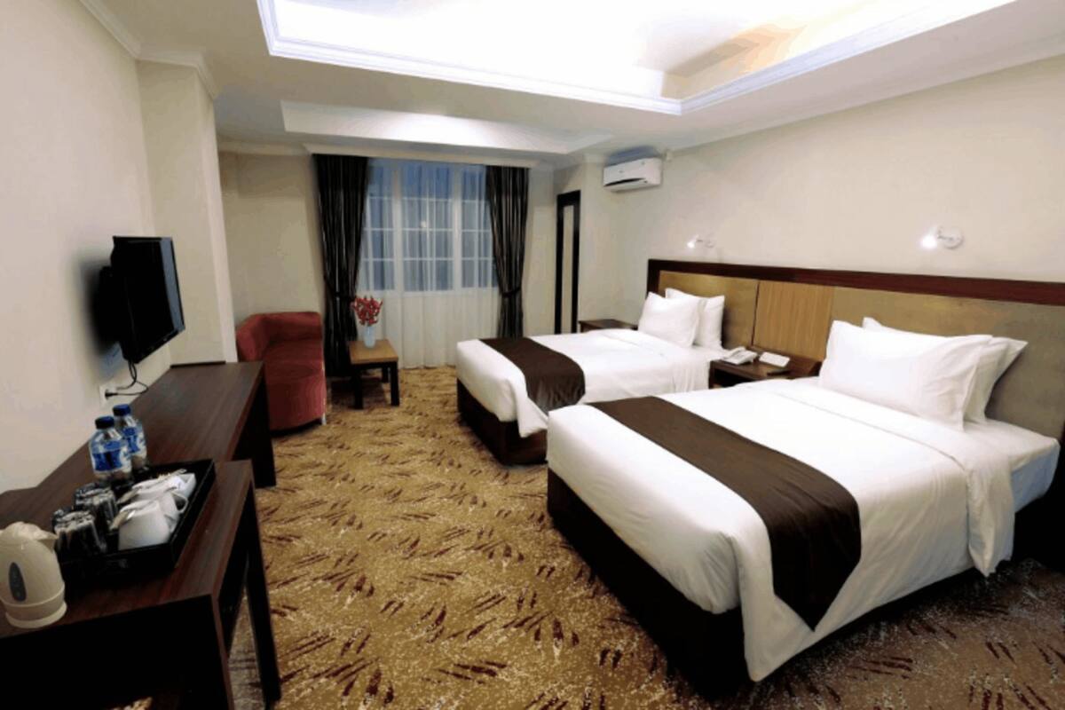 Ein Hotelzimmer mit zwei Betten, einem Schreibtisch, einem Fernseher, einem Stuhl und einem Fenster mit Vorhängen.
