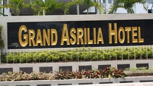 Ein Schild für das Grand Asrilia Hotel mit modernem Design und einer Reihe Pflanzen davor.