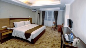 Ein Hotelzimmer mit einem großen Bett, einem Schreibtisch mit Stuhl, einem Fernseher und einem Fenster mit Vorhängen.
