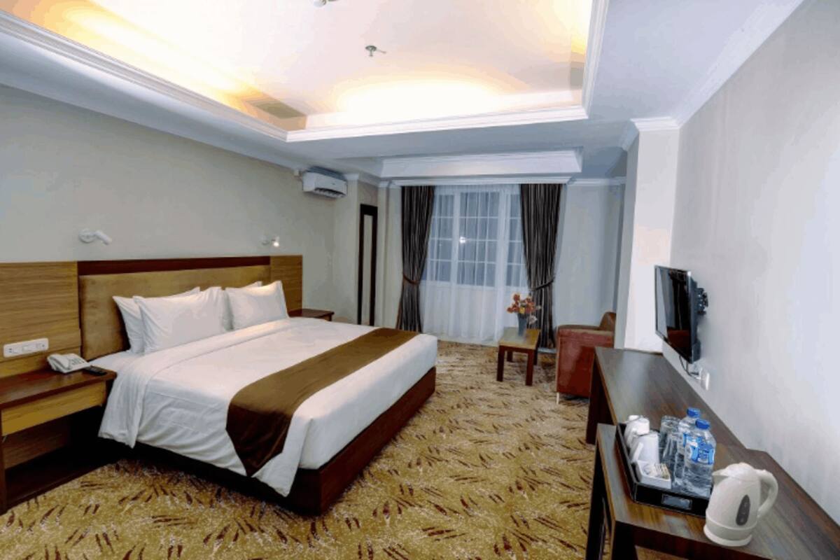 Ein Hotelzimmer mit einem großen Bett, einem Schreibtisch mit Stuhl, einem Fernseher und einem Fenster mit Vorhängen.