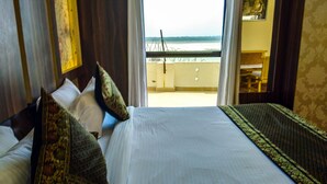 Habitación de hotel con cama, almohadas y vista al mar desde un balcón.
