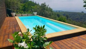 A rectangular pool with a wooden deck and potted plants, surrounded by lush greenery and a scenic view. - SestoSenso Suites (Campiglia Marittima)