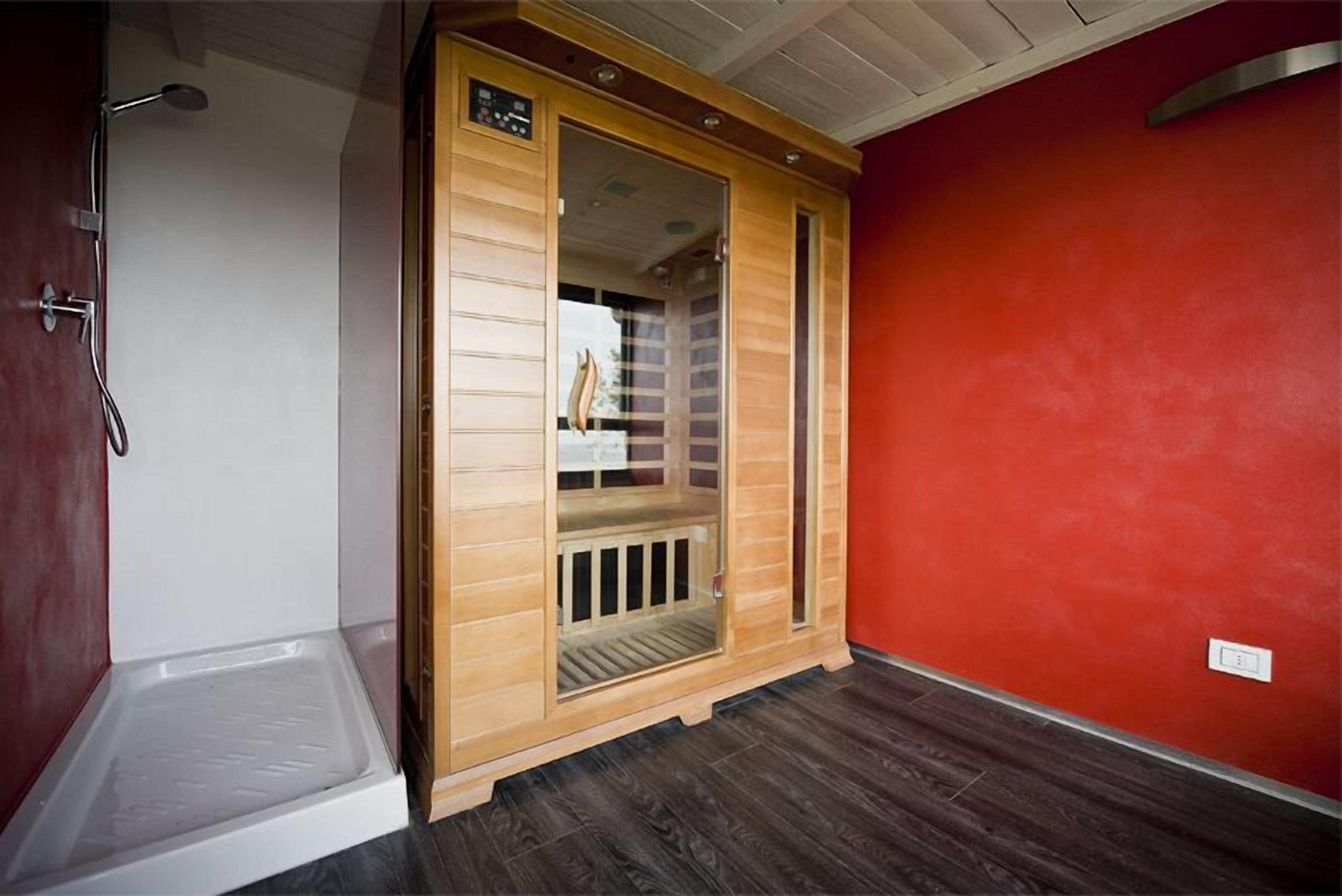 Ein Saunaraum mit Holztür, einer Sitzbank im Inneren und einer Dusche links.