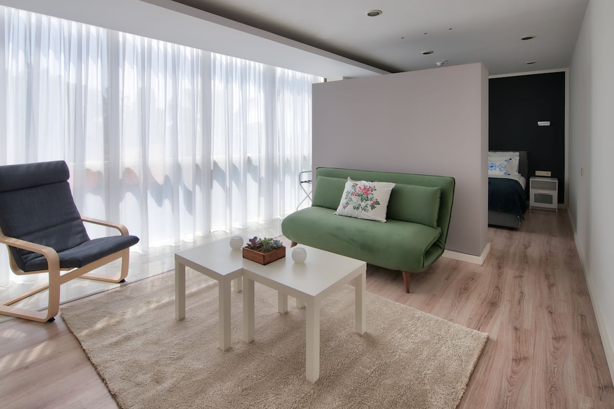A modern living room with a green sofa, a dark blue chair, a white coffee table, and a large window with sheer curtains.