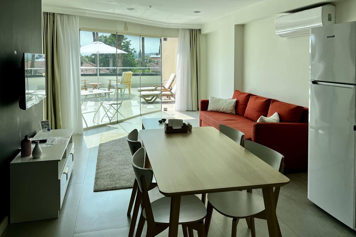 A modern kitchen with a dining area, a sofa, and a large window with a view of the outdoors.