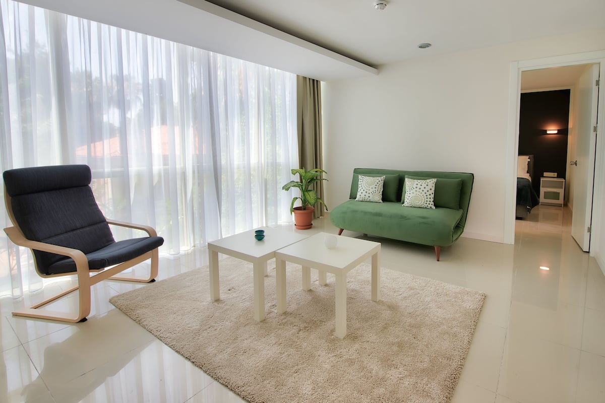 A modern living room with a large window, a green sofa, a white coffee table, and a blue chair.