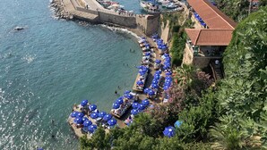 A coastal area with a stone pier, boats, and a row of blue umbrellas along the waterfront. - Arkk Homes (Antalya)