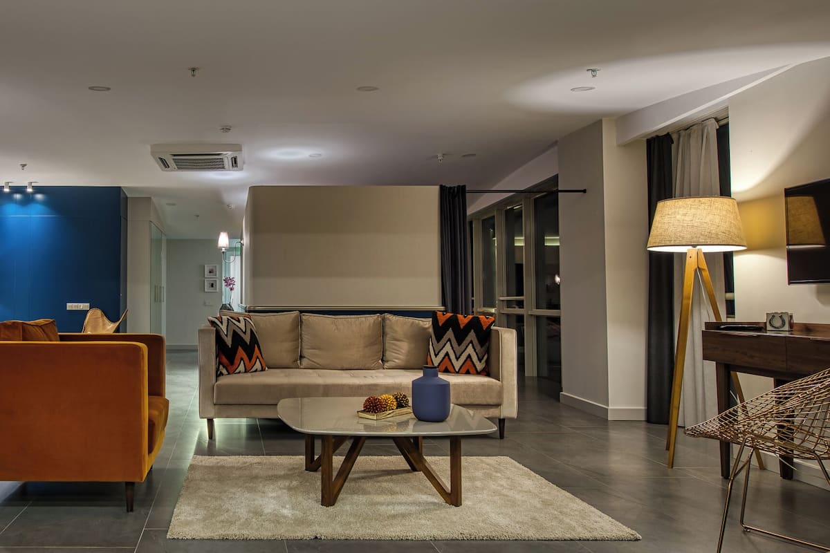 A modern hotel lobby with a dining area, sofa, coffee table, and a TV.