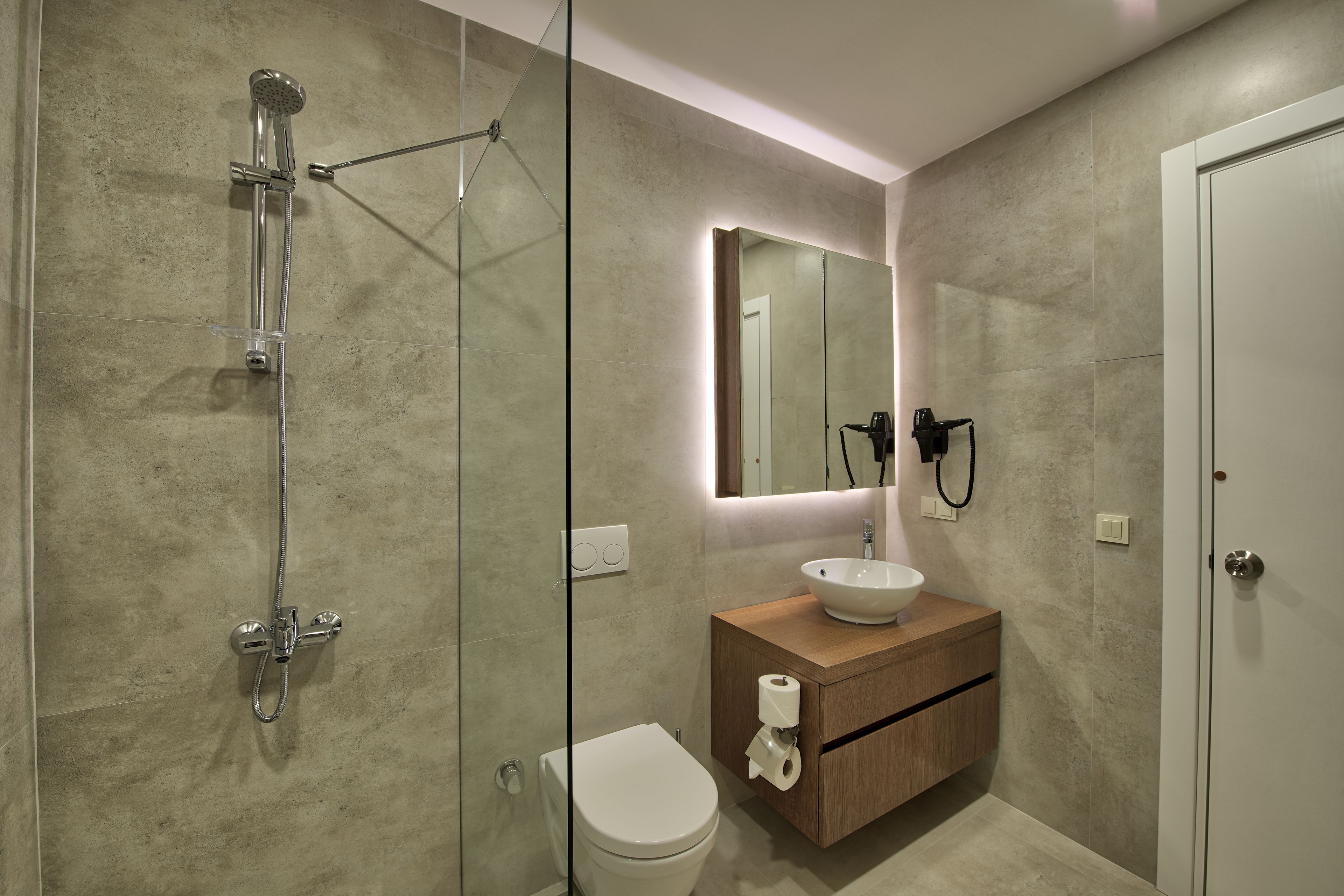 Ein modernes Badezimmer mit einer gläsernen Dusche, einer weißen Toilette, einem Holzwaschtisch und einem großen Spiegel.