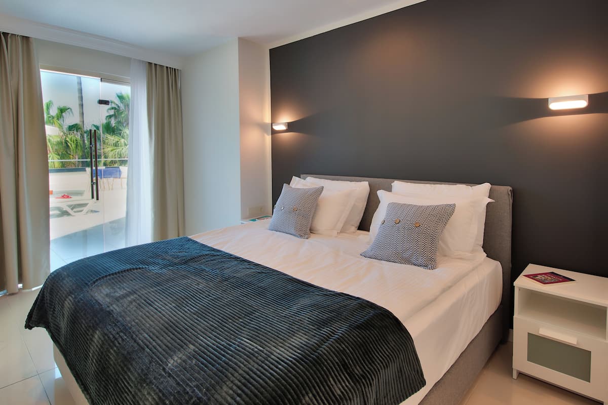 A hotel room with a large bed, a nightstand, and a view of palm trees through the glass door.