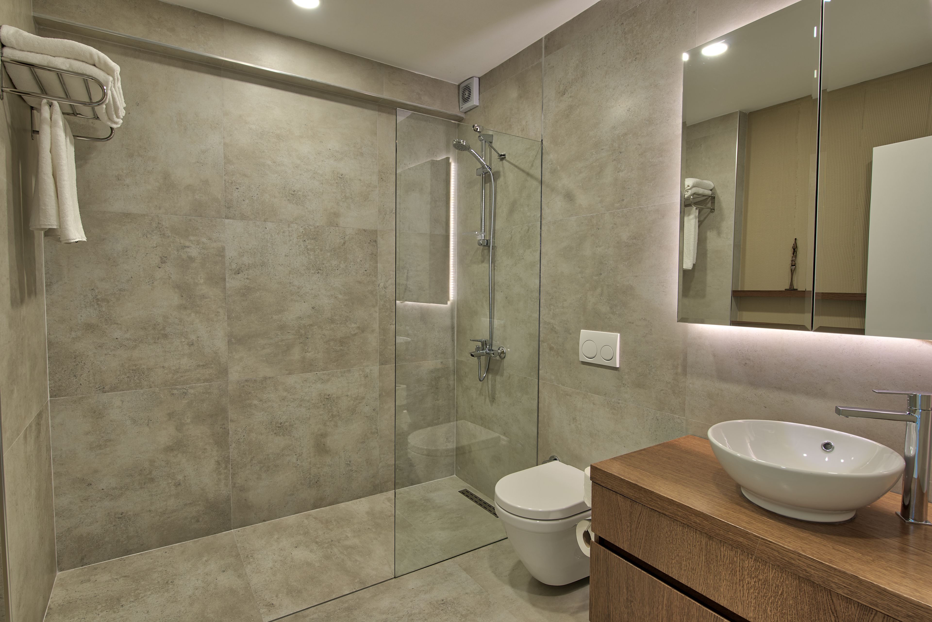 Un baño moderno con ducha de vidrio, inodoro blanco y tocador de madera con lavamanos sobre la superficie.