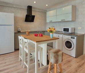 A modern kitchen with a wooden table, white chairs, a washing machine, and a microwave. - Arkk Homes (Antalya)
