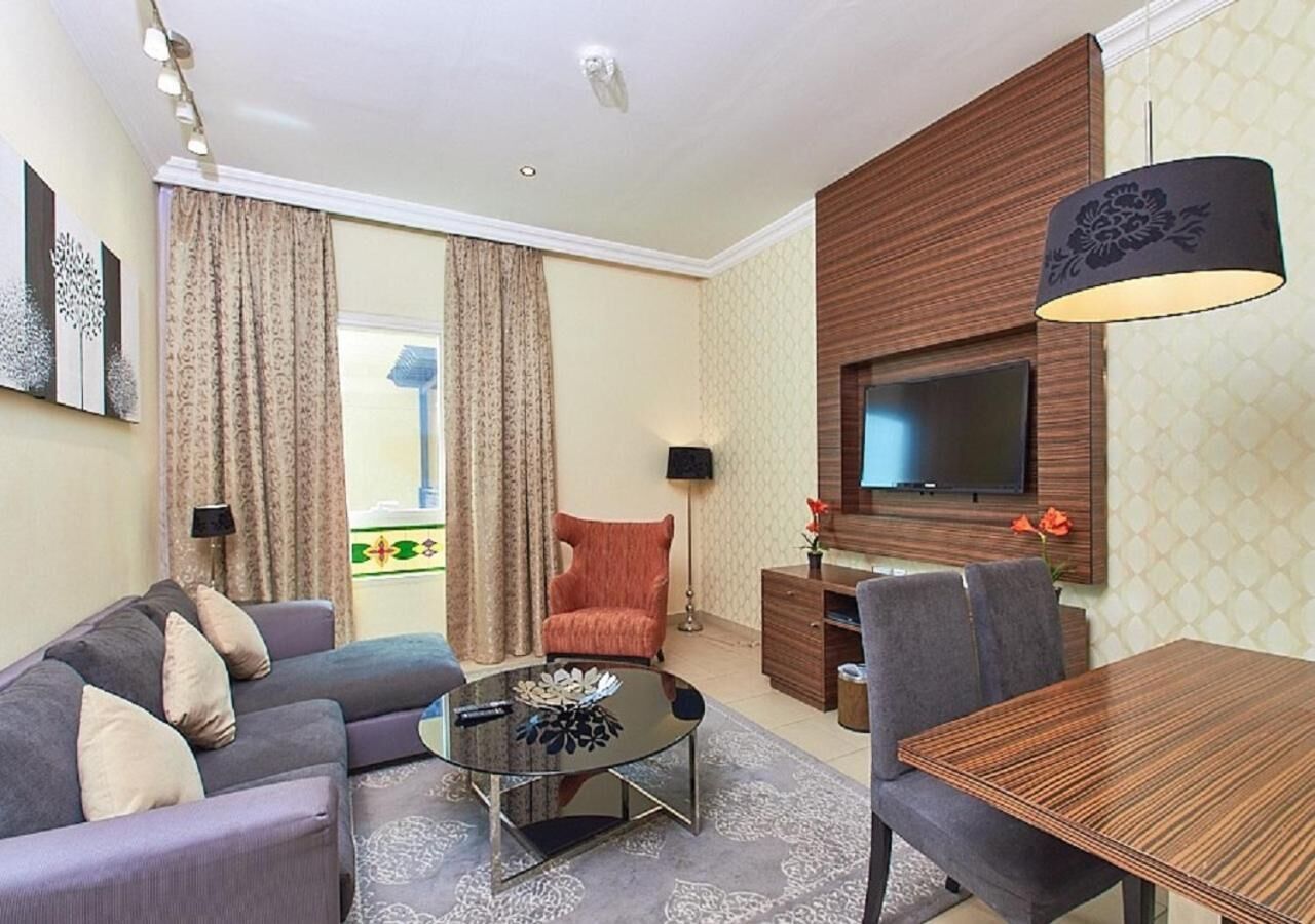 A modern living room with a sofa, armchairs, a coffee table, a TV mounted on the wall, and a dining table.