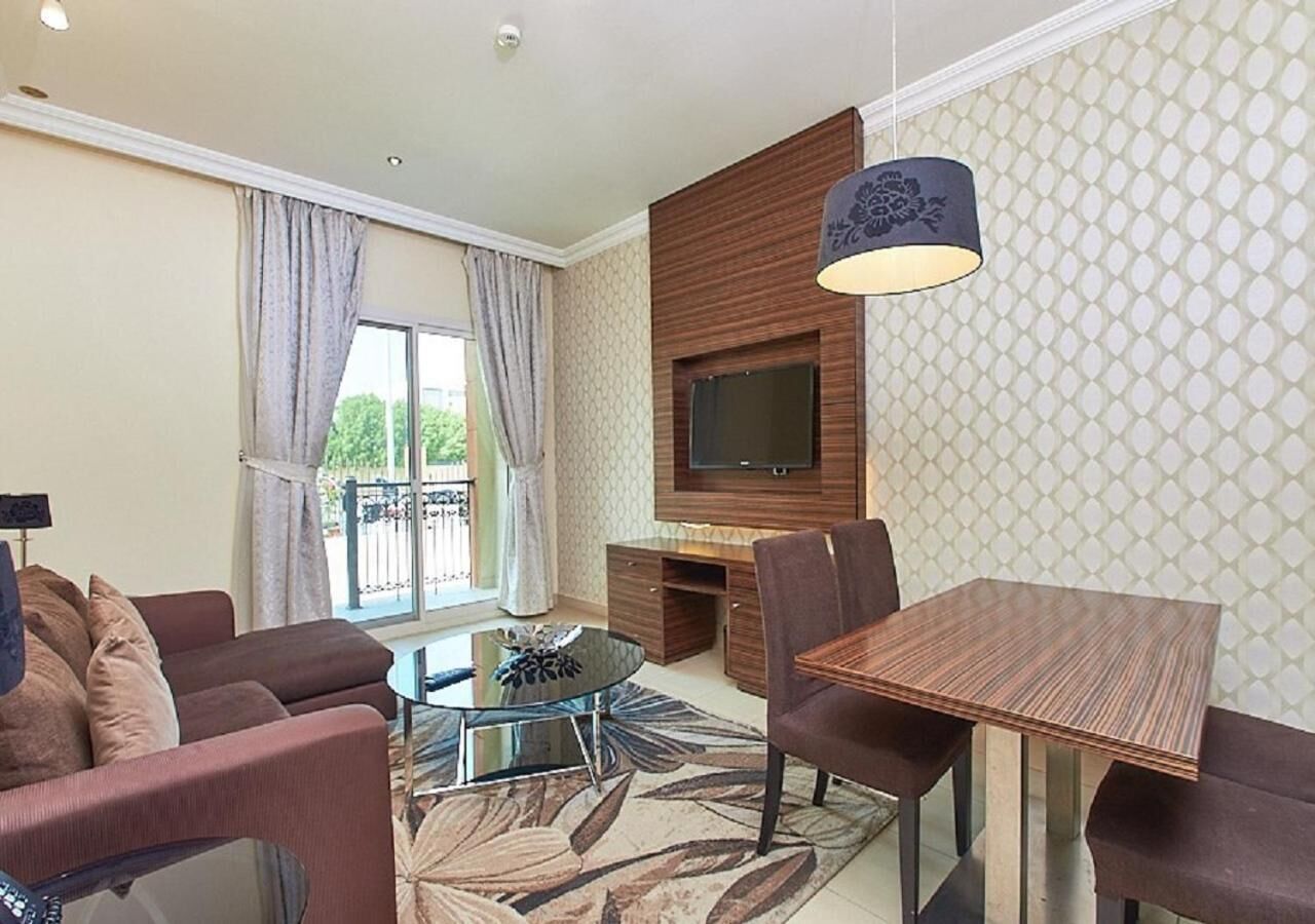 A modern living room with a sofa, a coffee table, a TV mounted on the wall, and a dining table with chairs.