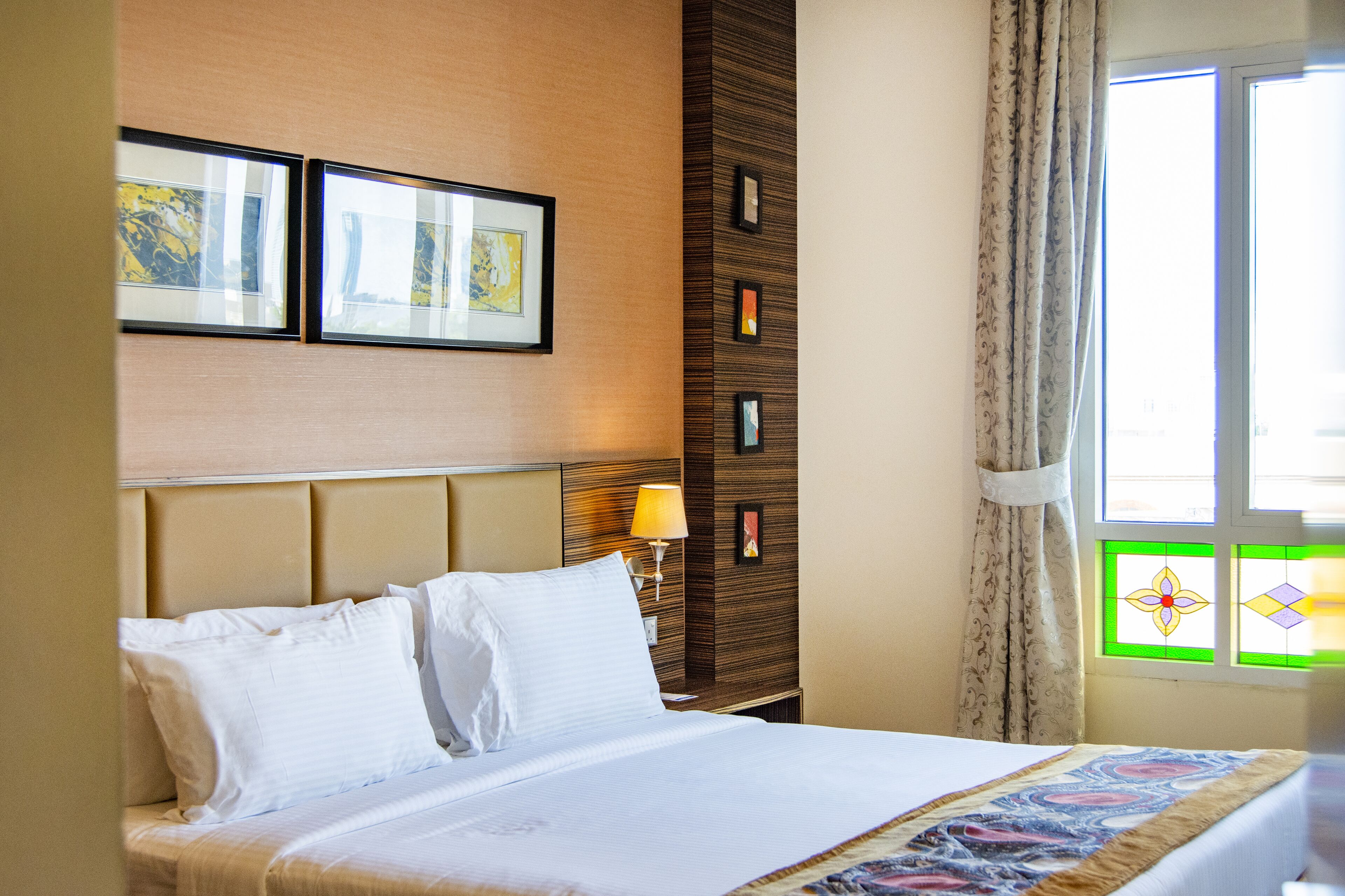 A hotel room with a bed, a nightstand, a lamp, and a window with curtains.