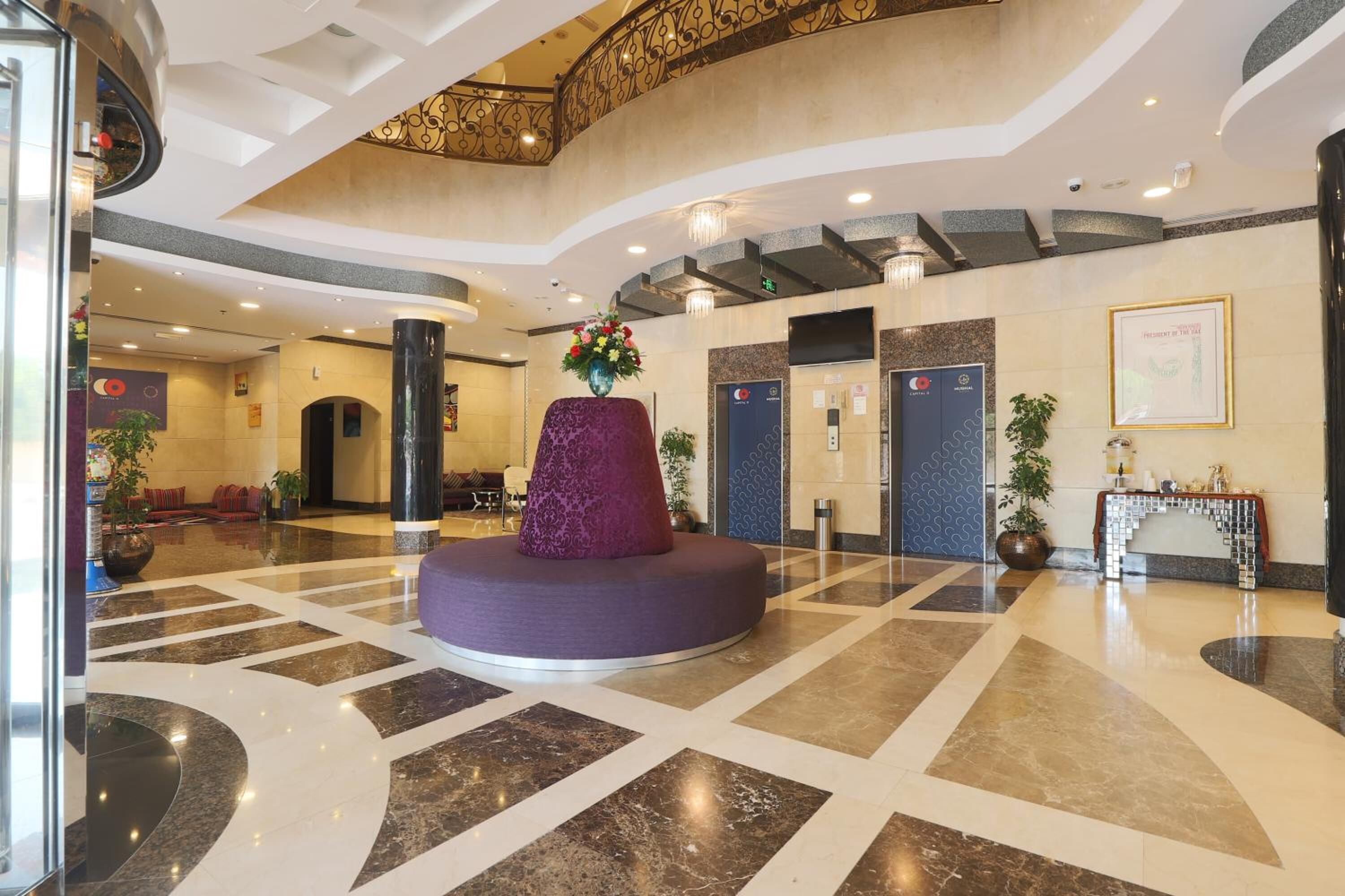 Un vestíbulo amplio con una zona de estar central, un mostrador de recepción y una escalera que lleva a un nivel superior.