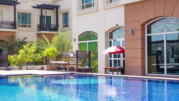 A swimming pool with a tiled edge, surrounded by a building with multiple balconies and large windows. - Mughal Suites (Ras Al Khaimah)