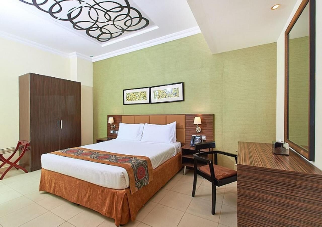Een hotelkamer met een groot bed, een houten kledingkast, een bureau met stoel en een spiegel aan de muur.