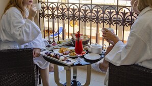 Two people seated at a table with breakfast items, a drink, and a basket of bread. - Mughal Suites (Ras Al Khaimah)