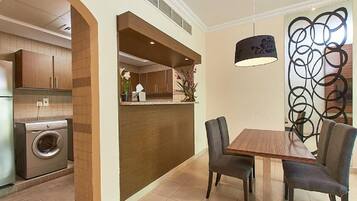 A modern kitchen with a built-in washer and dryer, a wooden dining table with chairs, and a decorative wall piece.