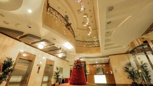 A spacious lobby with a central red floral arrangement, a curved staircase, and a reception desk. - Mughal Suites (Ras Al Khaimah)